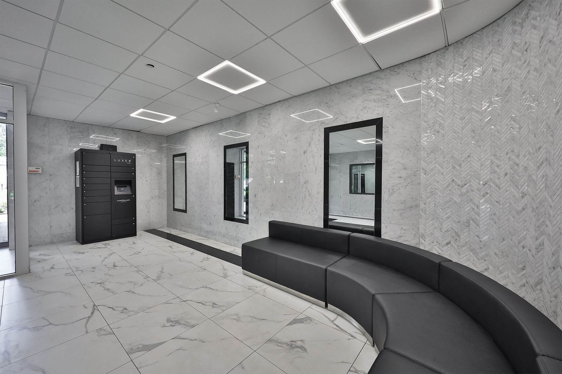 Interior community lobby with marble walls, curved black sofa, and a parcel locker area.