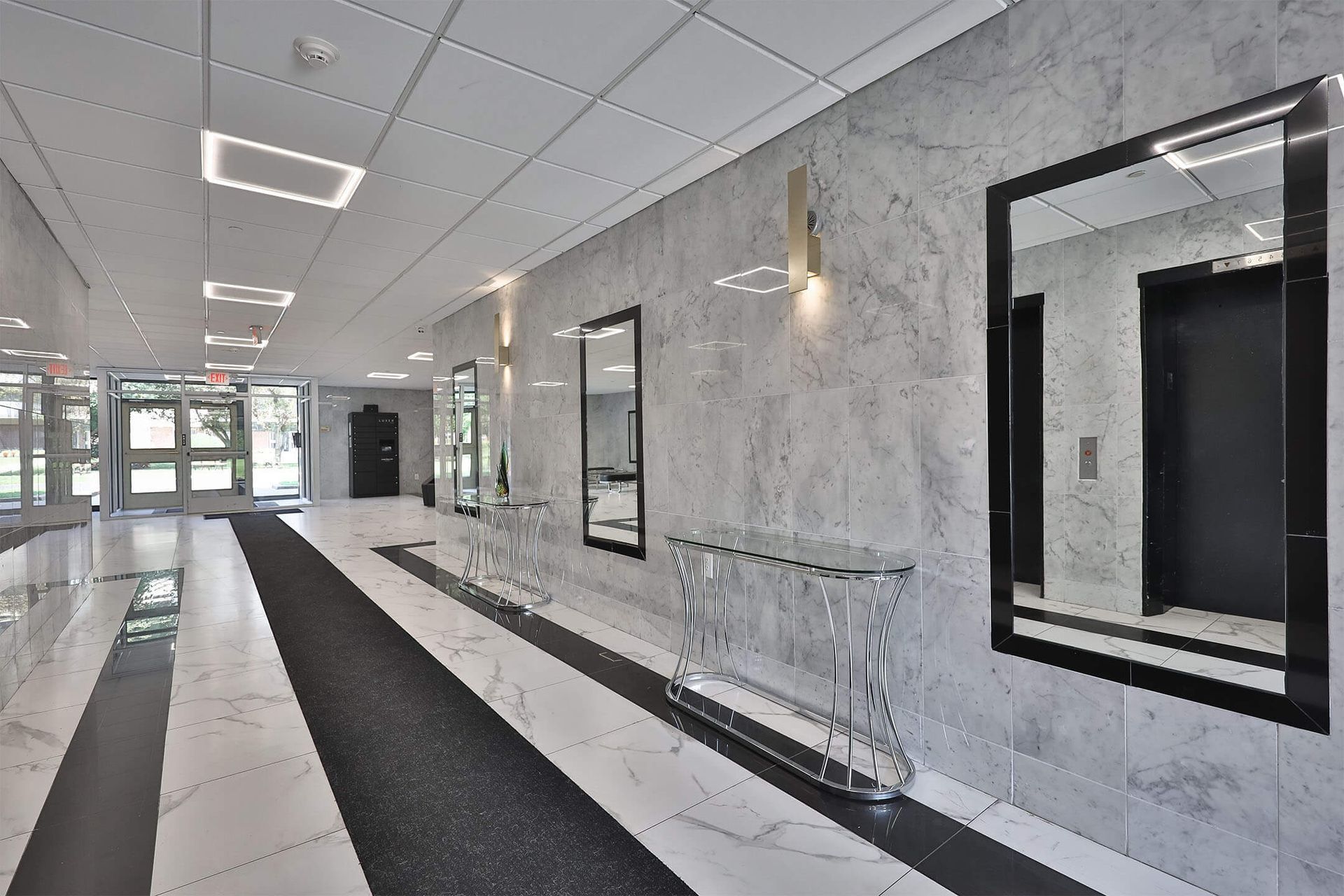 Marble lobby with mirrors, metal console tables, and entry doors.