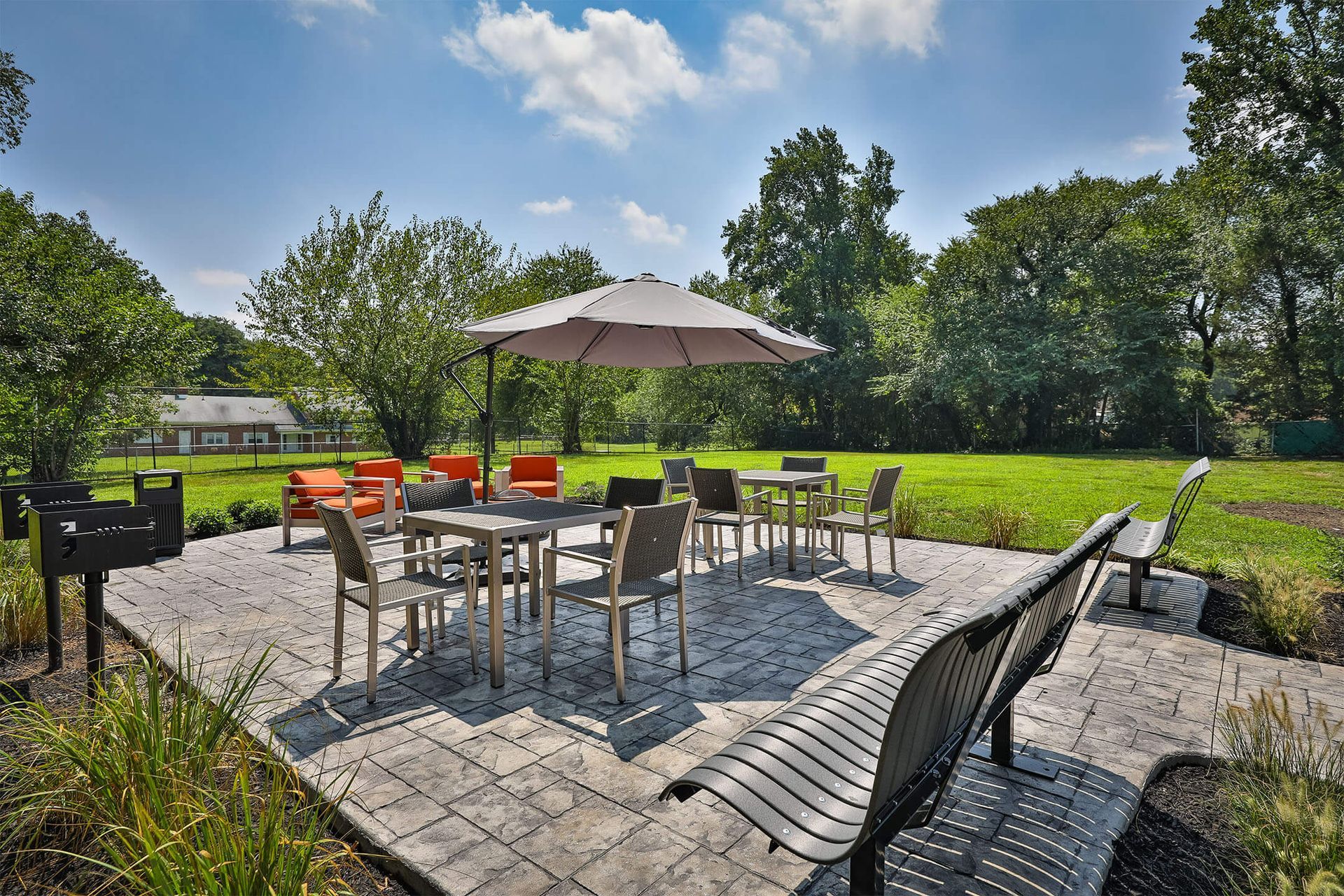 Outdoor communal patio with tables, chairs, and a large umbrella on a stone deck.