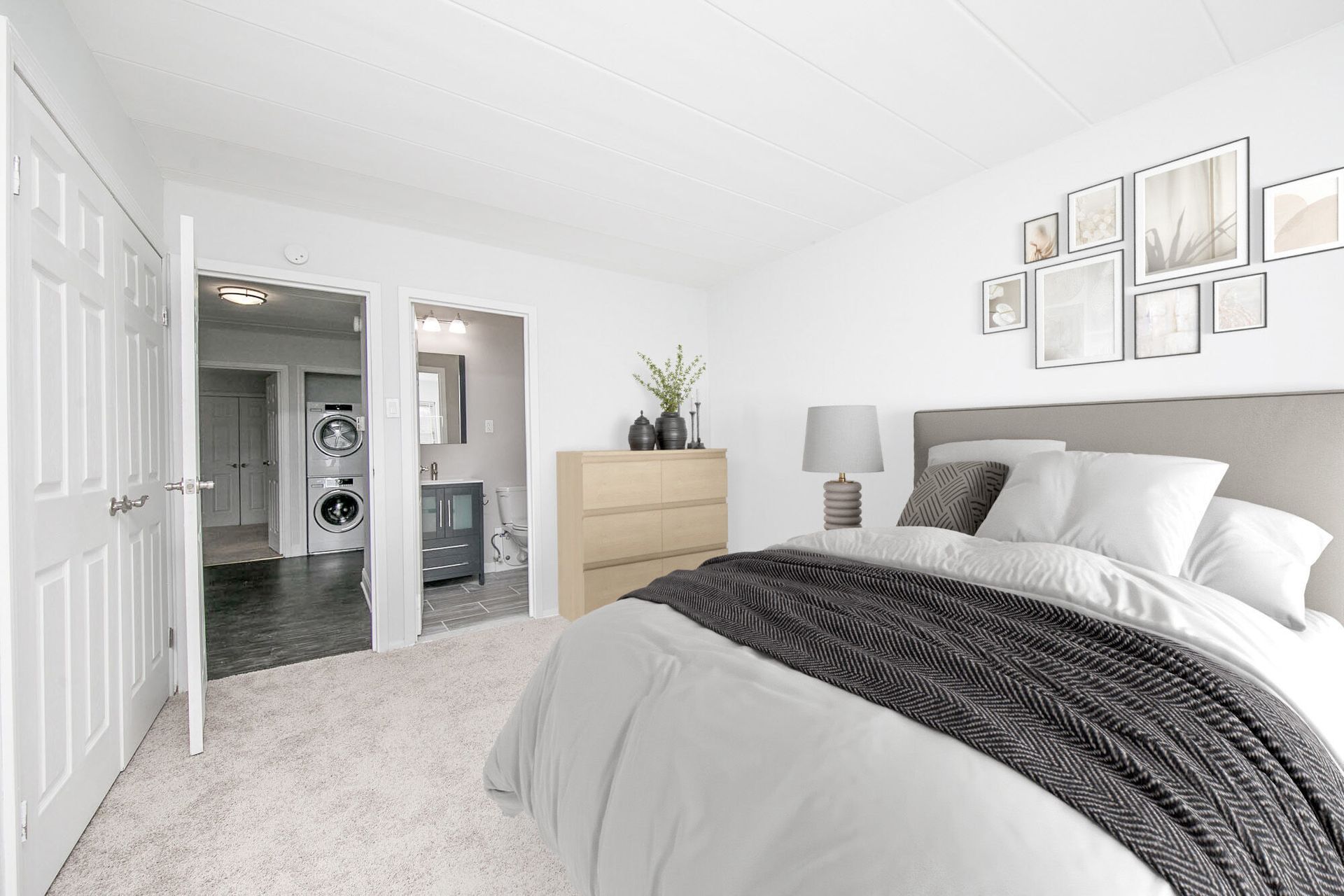 Bedroom with bed, dresser, and doorway to laundry area. White walls, soft carpet.