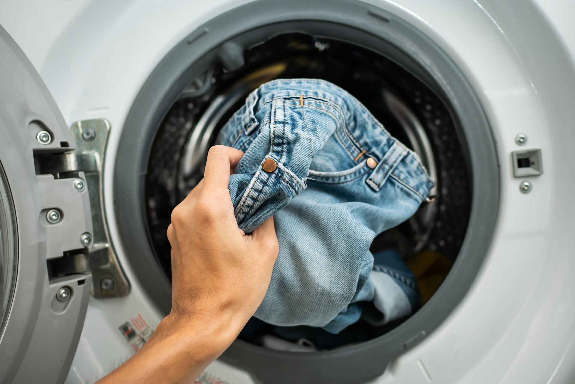 Hand loading denim jeans into a front-loading washing machine.