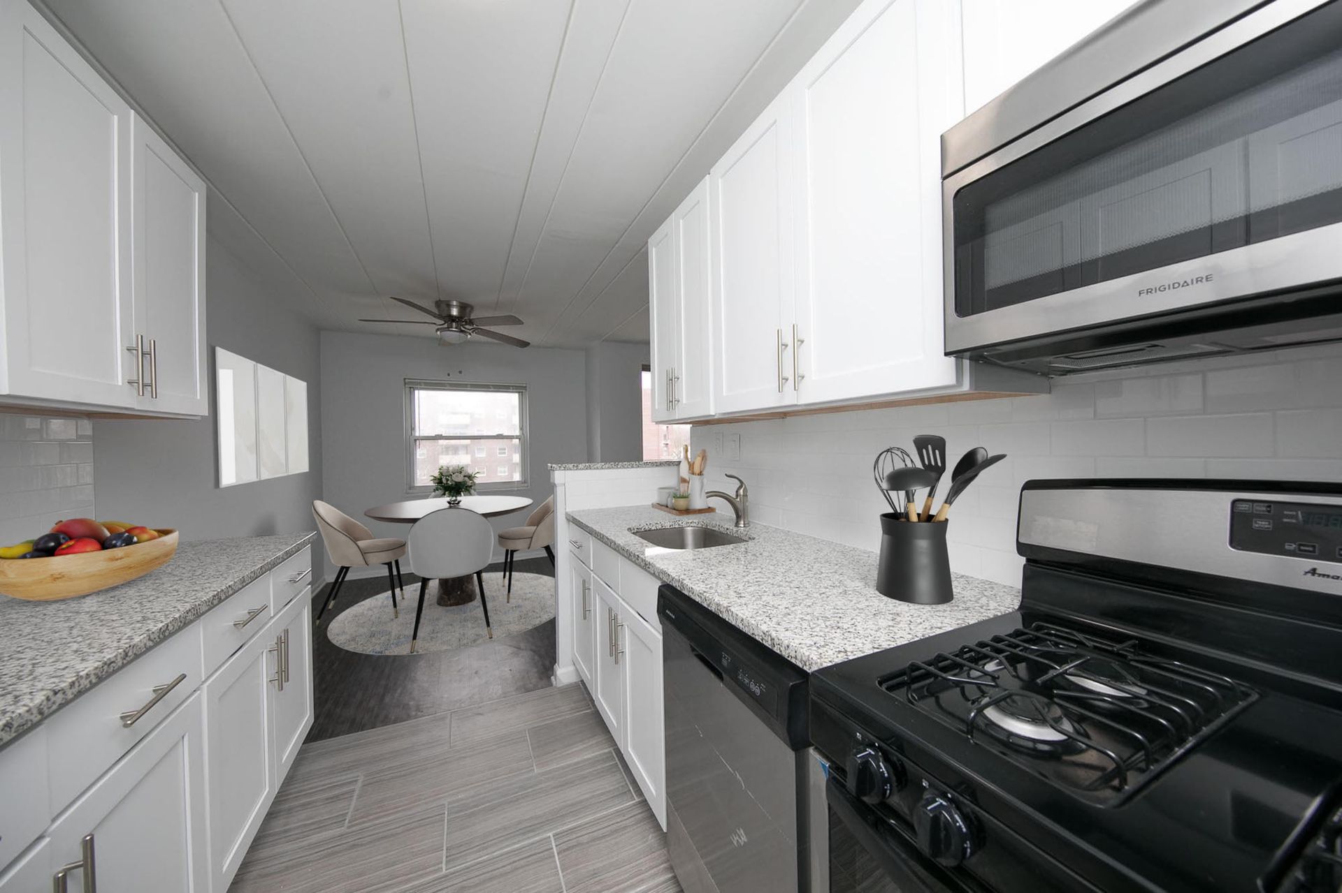 Bright white kitchen with granite countertops, white cabinets, stainless steel appliances, and a small dining area in the back.