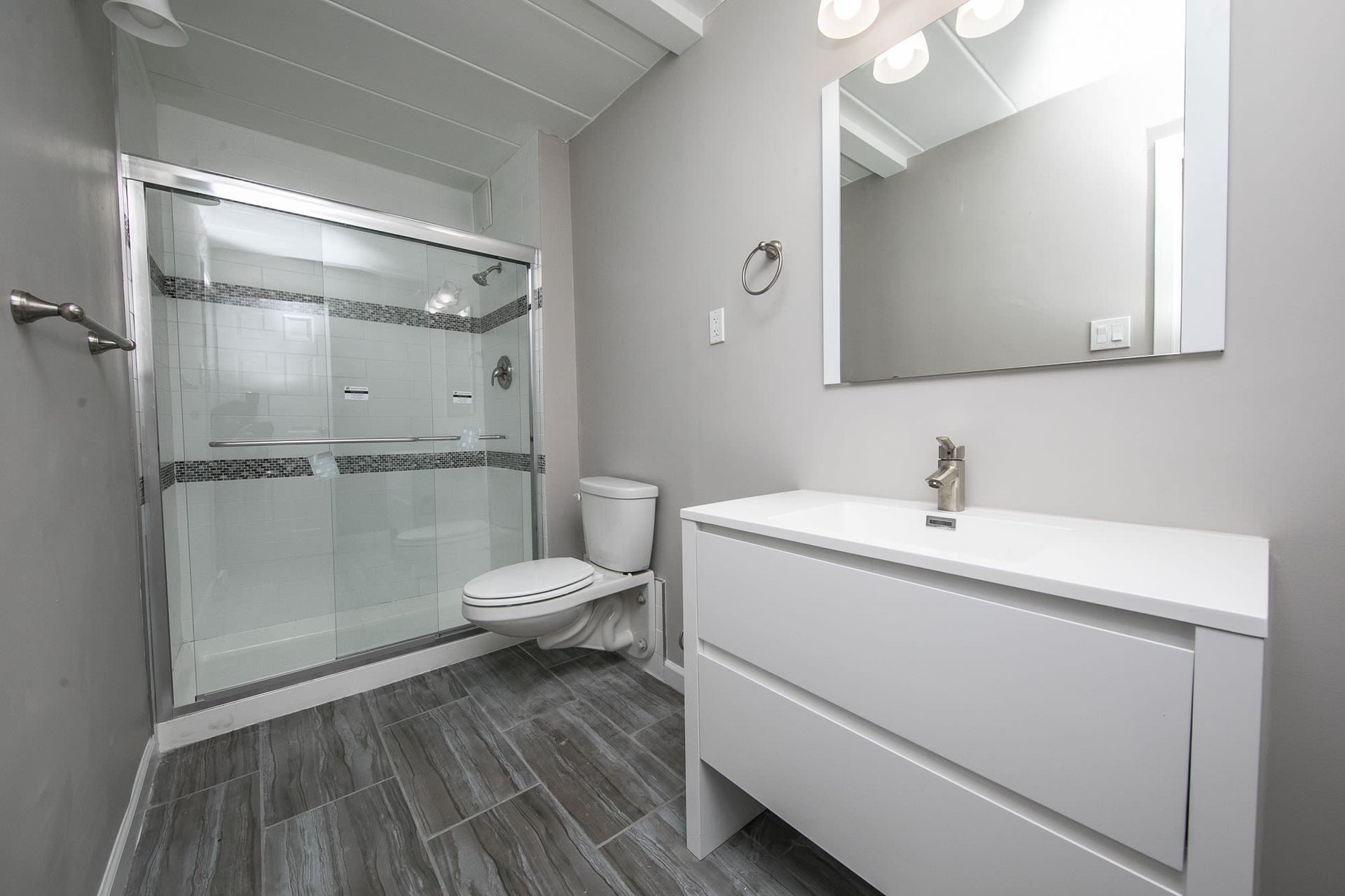 Modern apartment bathroom with glass-enclosed shower, toilet, and vanity.