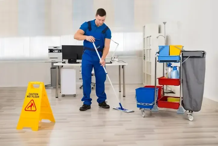 A man is mopping the floor in an office next to a caution sign.