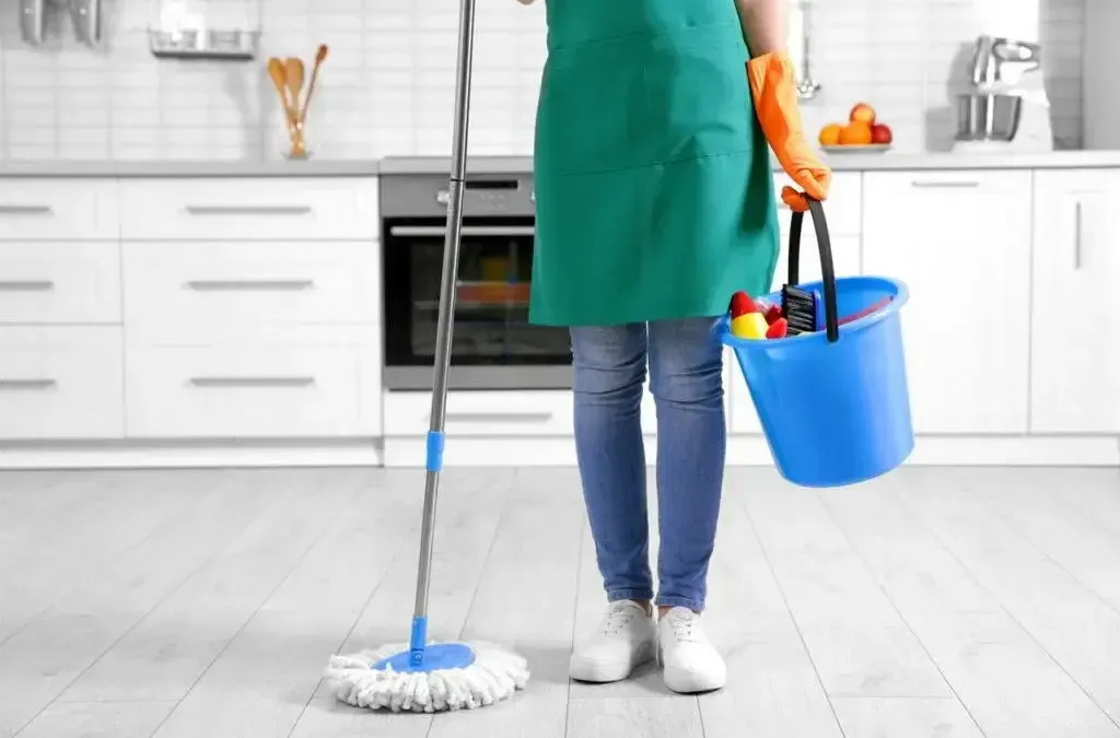 A woman is cleaning the floor in a kitchen with a mop and bucket.