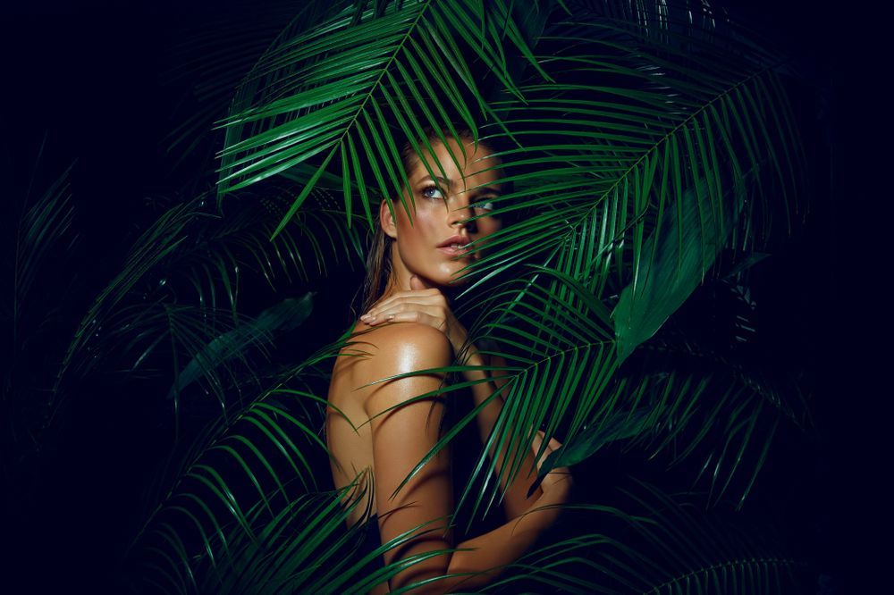 A woman is standing in the jungle surrounded by palm leaves.