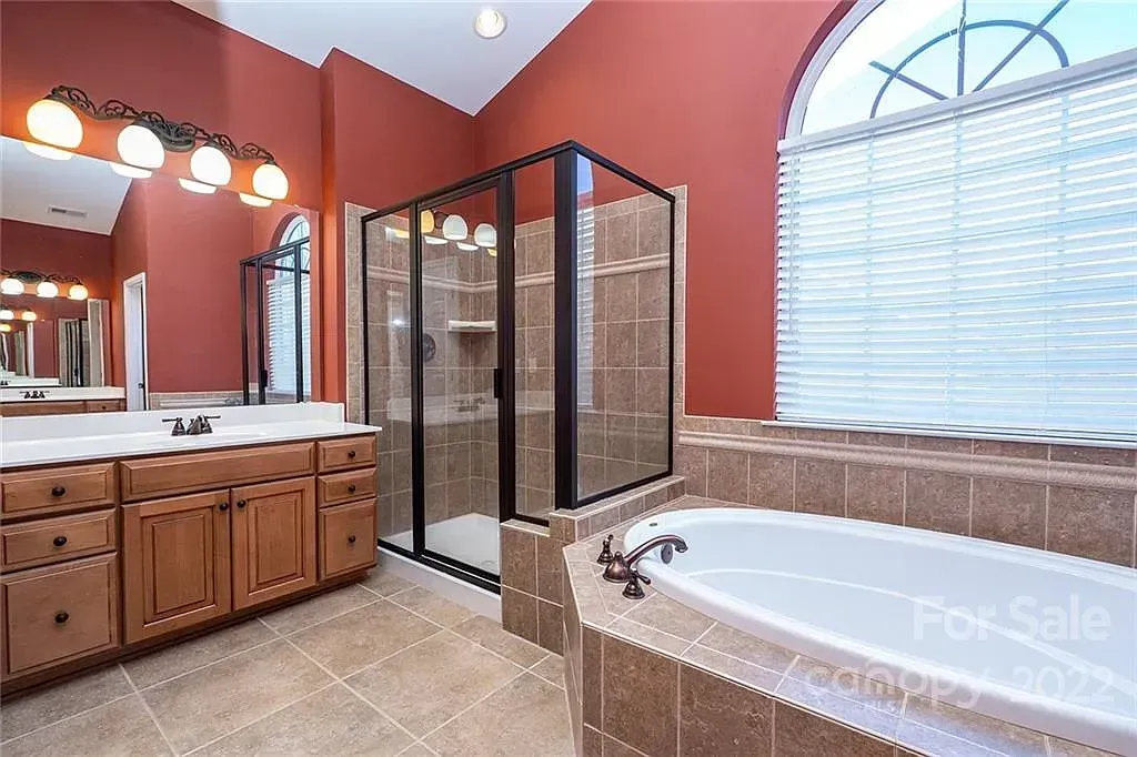 Spacious bathroom with a tub, shower, and vanity. Red walls, brown tile, and large window.