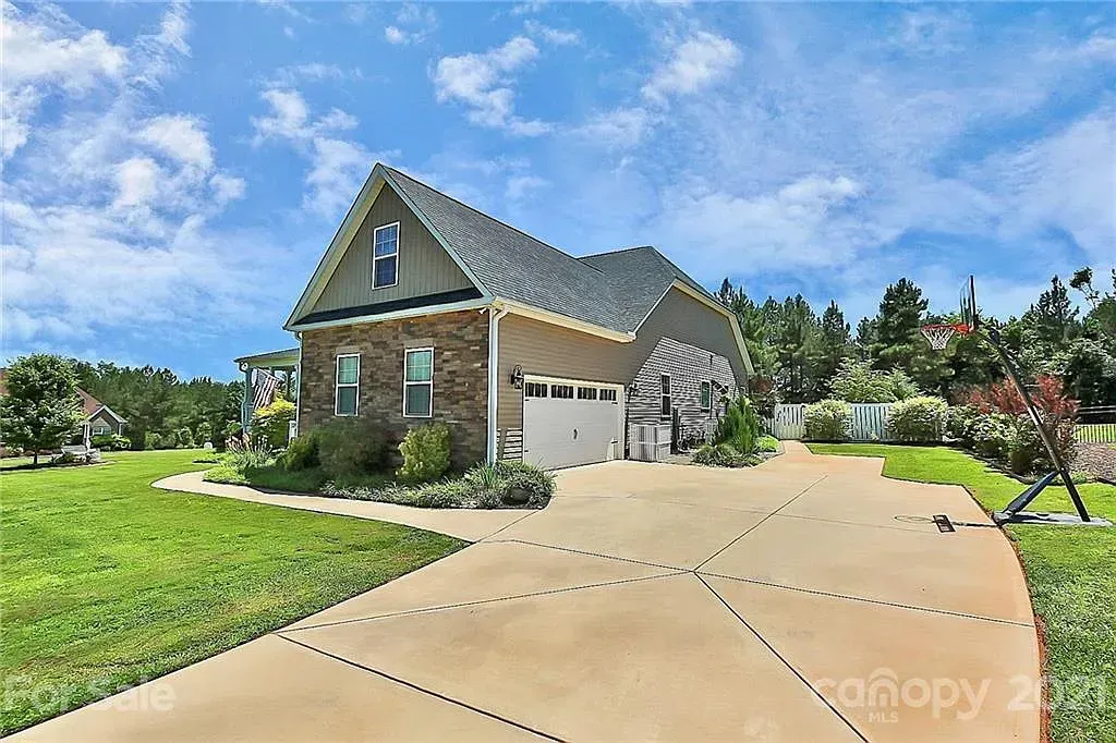 Brick and siding house with a two-car garage, driveway, and lawn against a blue sky.