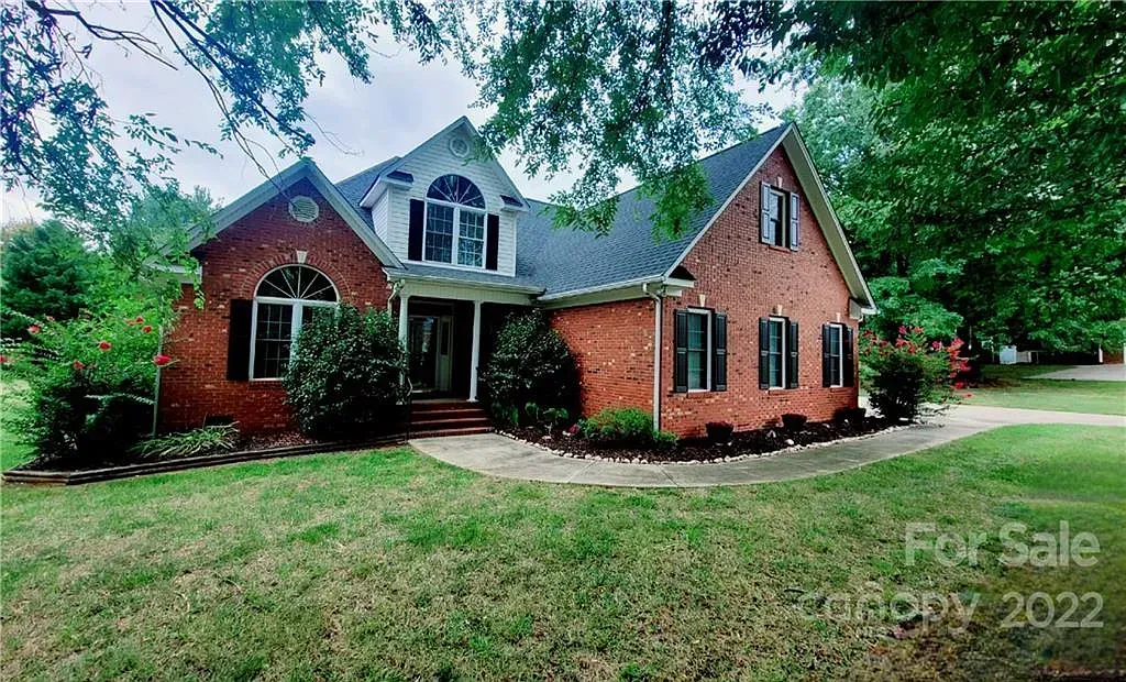 Red brick house with black shutters, surrounded by green lawn and trees; 