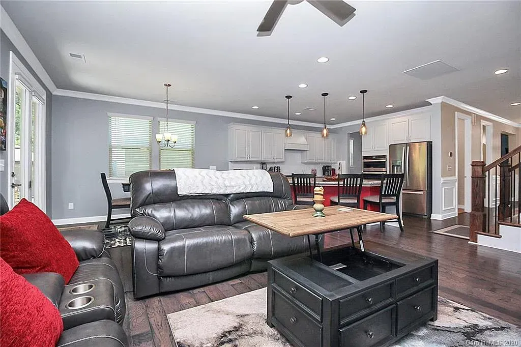 Open-concept living space with grey walls, a black leather couch, and kitchen with stainless steel appliances.