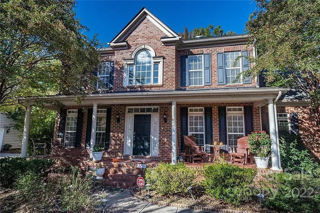 Two-story brick house with a porch, shutters, and trees in front.