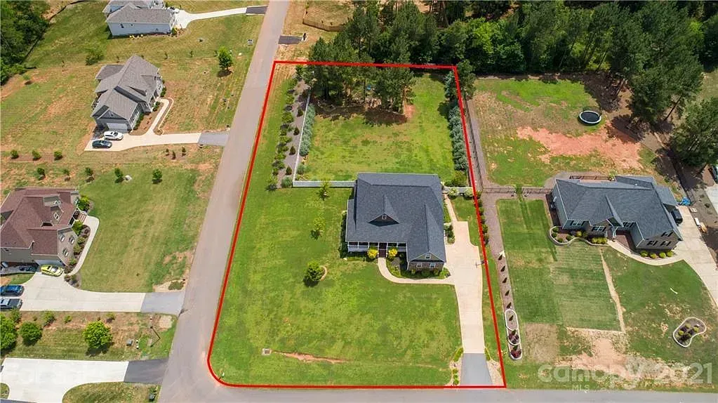 Aerial view of a house with a long driveway and manicured lawn; red border outlines the property.