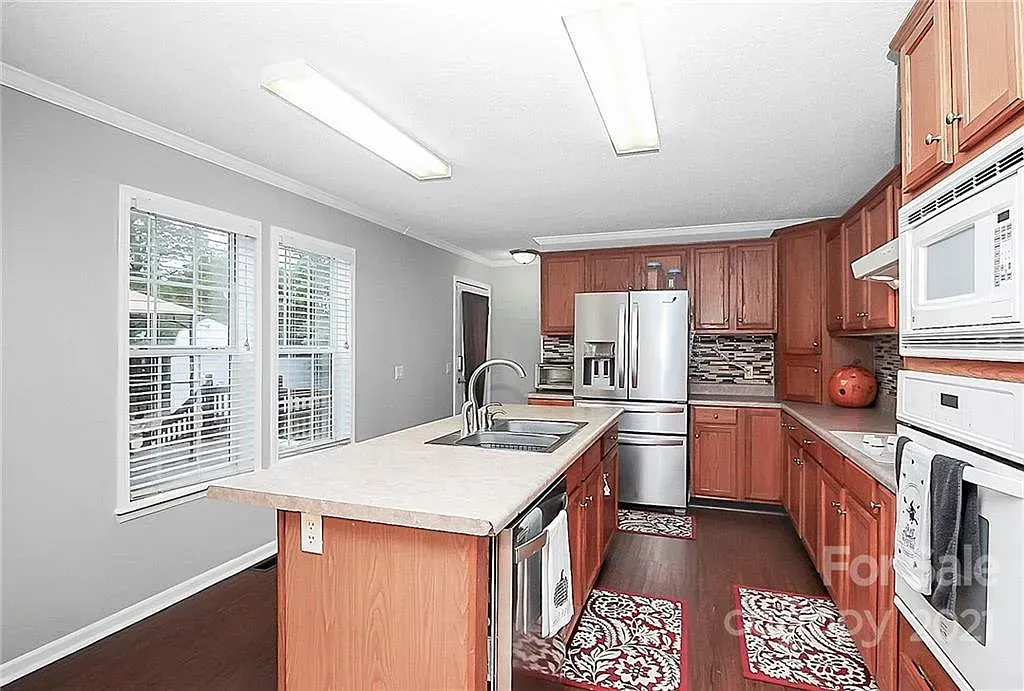 Kitchen with wood cabinets, stainless steel appliances, island, and dark flooring.