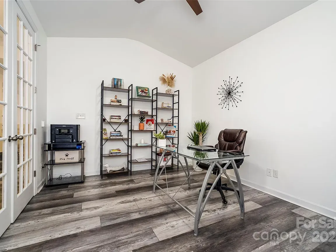 Home office with a desk, shelving, and double French doors, painted white, with gray wood-look flooring.