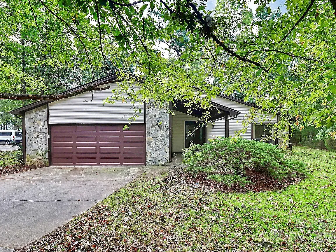 A one-story house with a brown garage door, stone accents, and a leafy green yard.