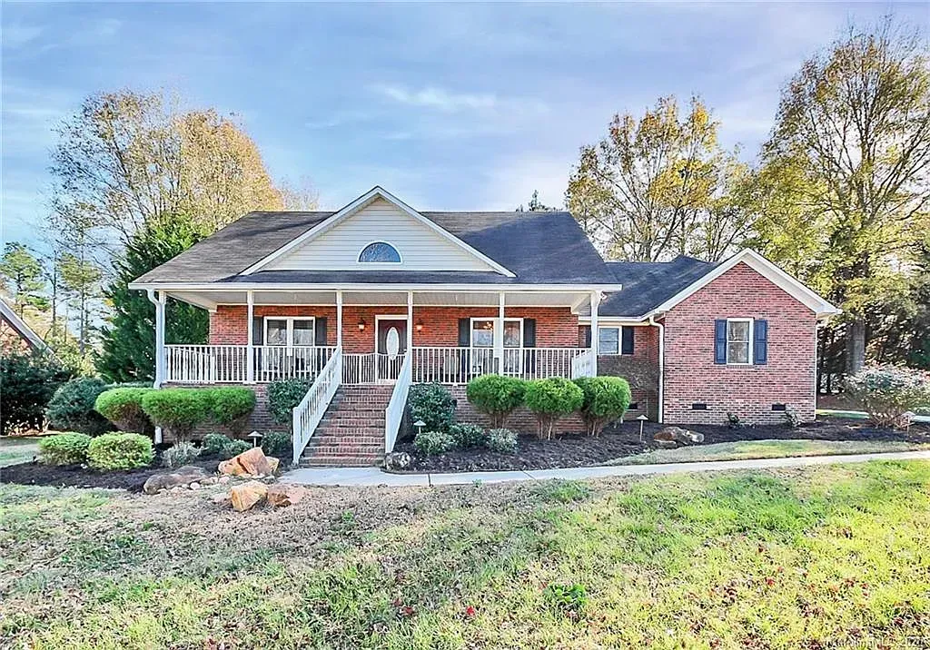 Brick house with porch, white trim, and green landscaping. Overcast sky in the background.