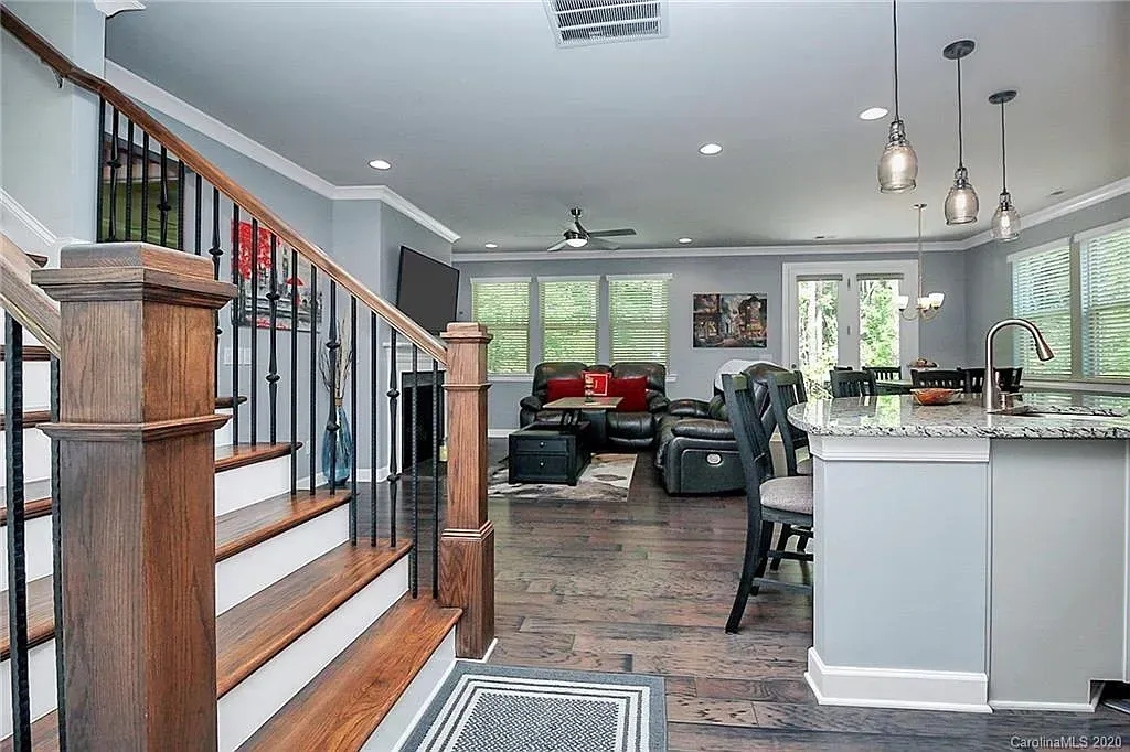 Open-concept living area with staircase, kitchen island, and living room; hardwood floors and gray walls.