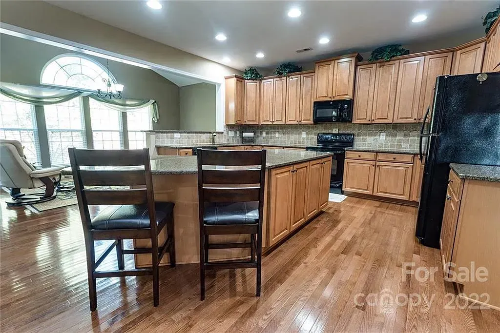 Kitchen with wood cabinets, island with stools, arched window, and light wood floors.