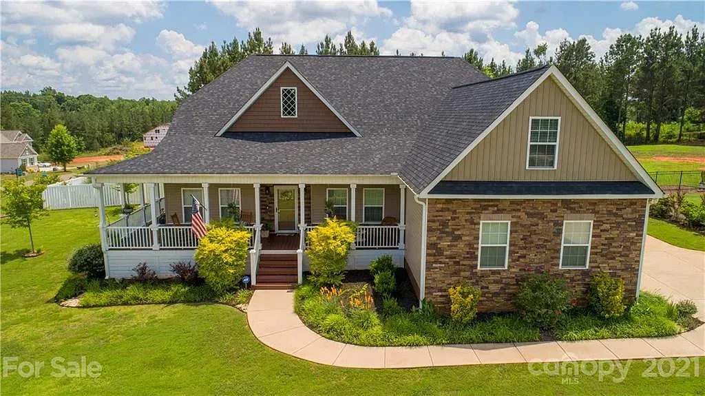House with stone facade and covered porch; lush green lawn, sunny day.