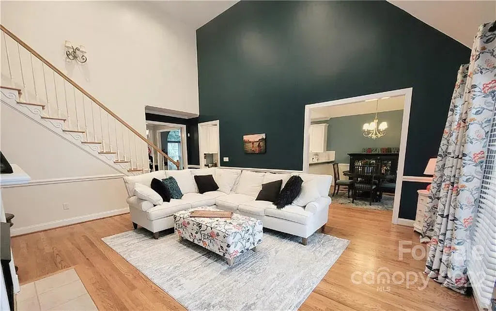 White sectional sofa in living room with a teal accent wall and staircase.