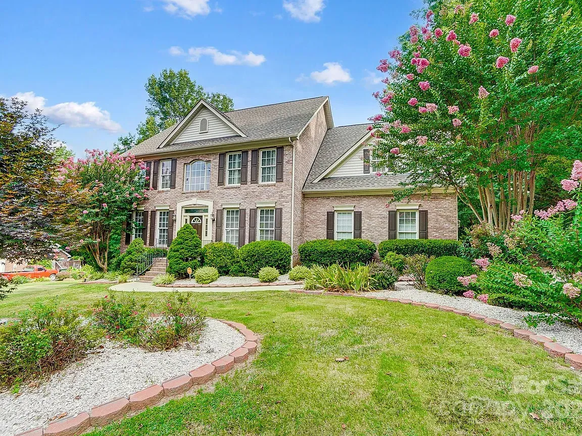 Two-story brick house with shutters and manicured landscaping under a blue sky.