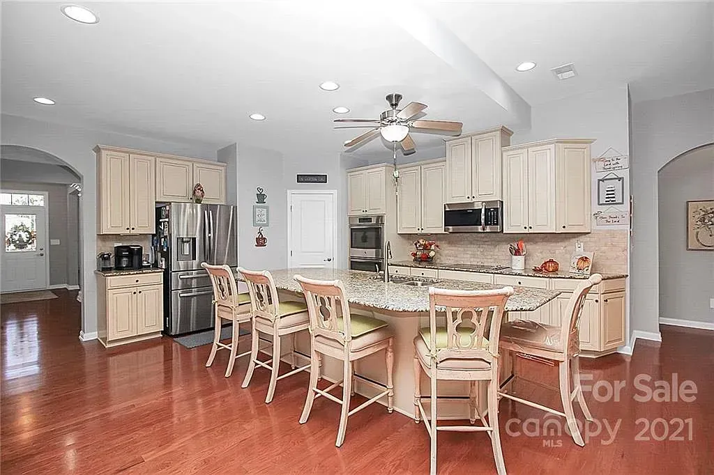 Kitchen with island seating, light wood cabinets, stainless steel appliances, and red wood floor.