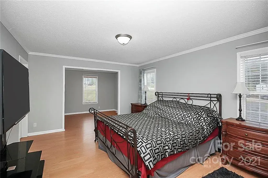 Bedroom with a bed, dresser, TV, and archway to another room, all in neutral colors.