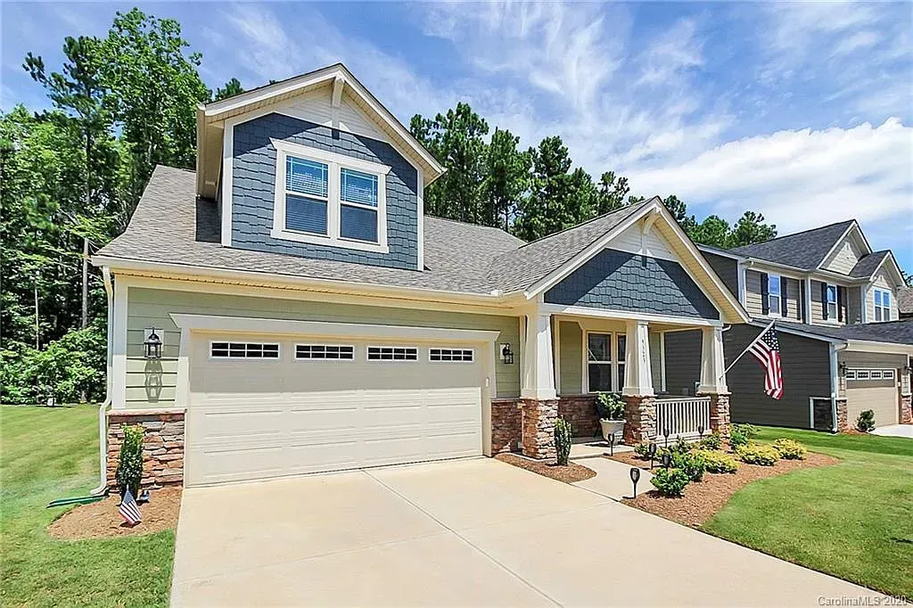Two-story house with garage, blue and beige siding, green lawn, blue sky, and trees.