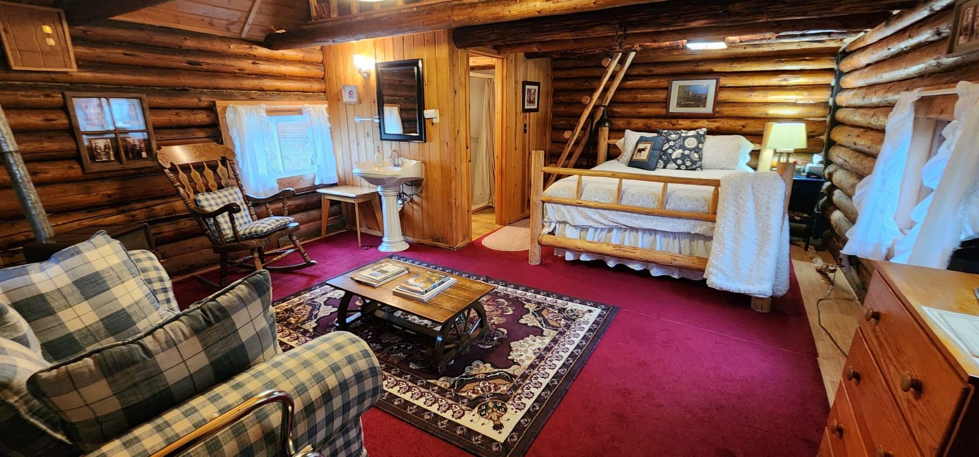 A living room in a log cabin with a couch , chair , table and bed.