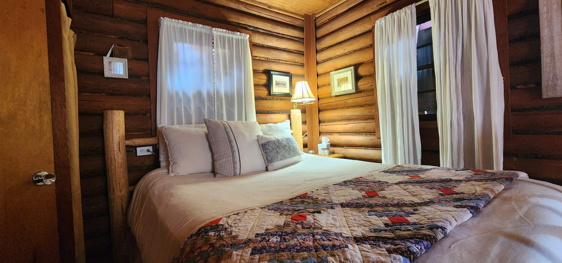 A bedroom in a log cabin with a bed and curtains.