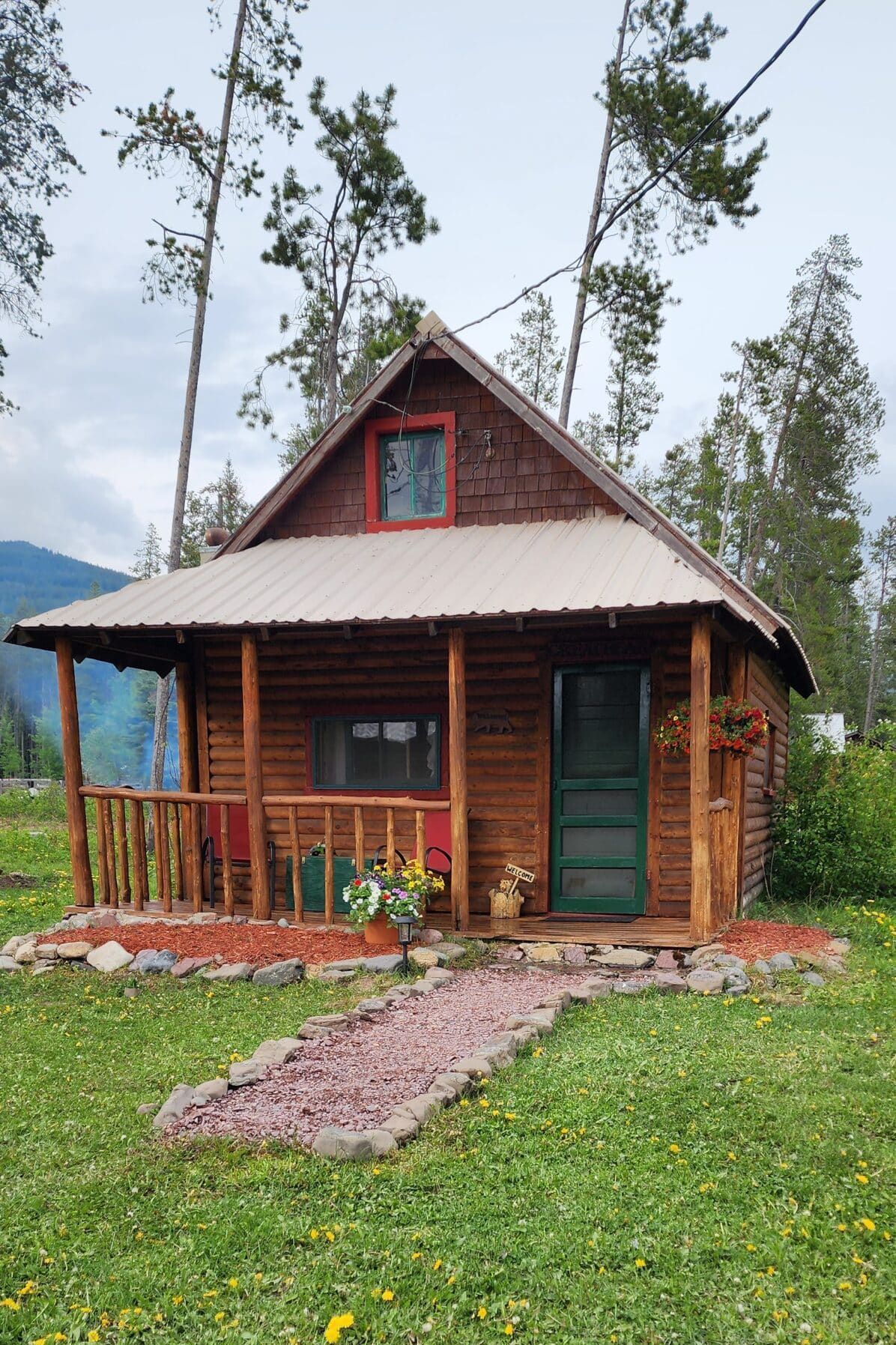 A small log cabin with a porch in the middle of a grassy field.