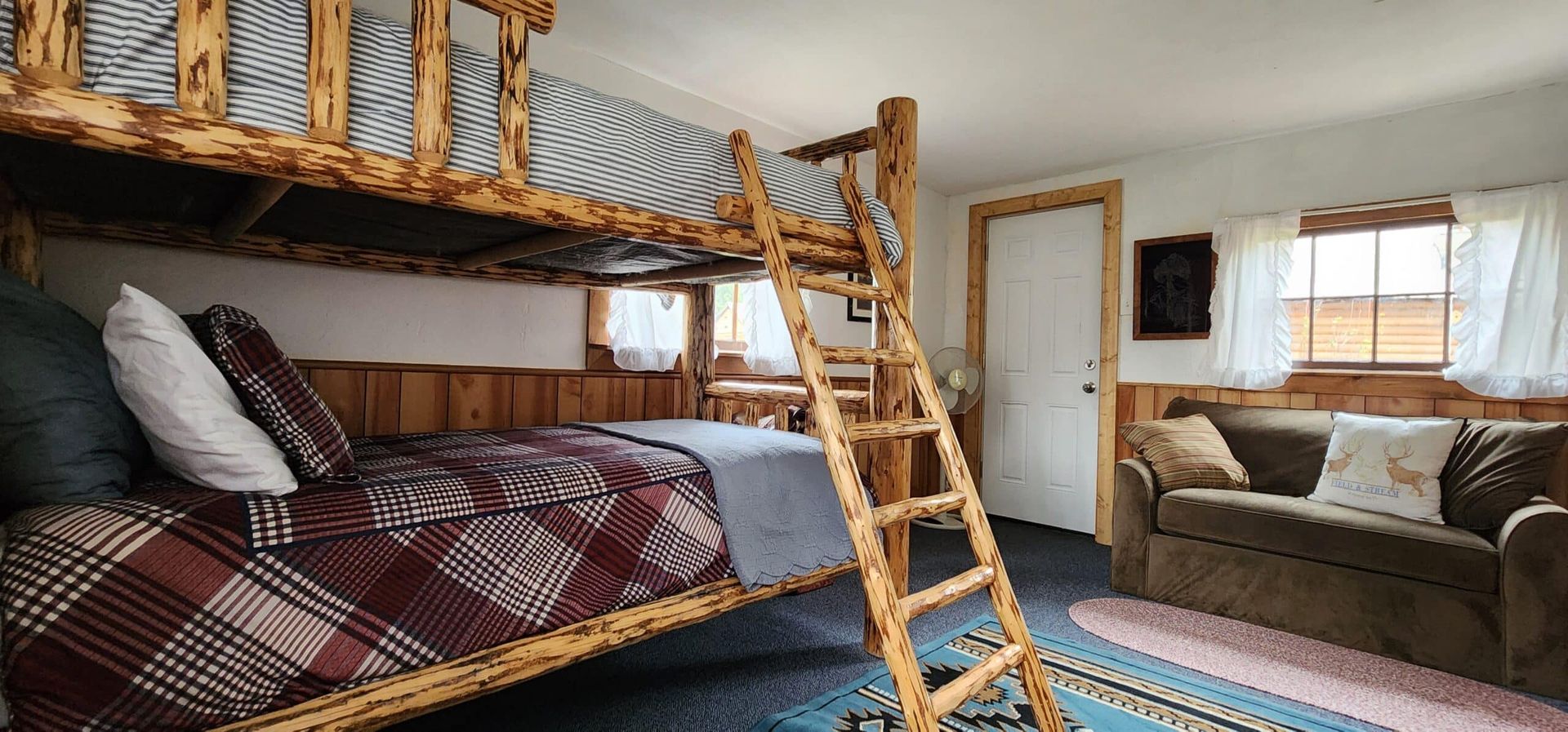 A bedroom with bunk beds , a couch , and a ladder.