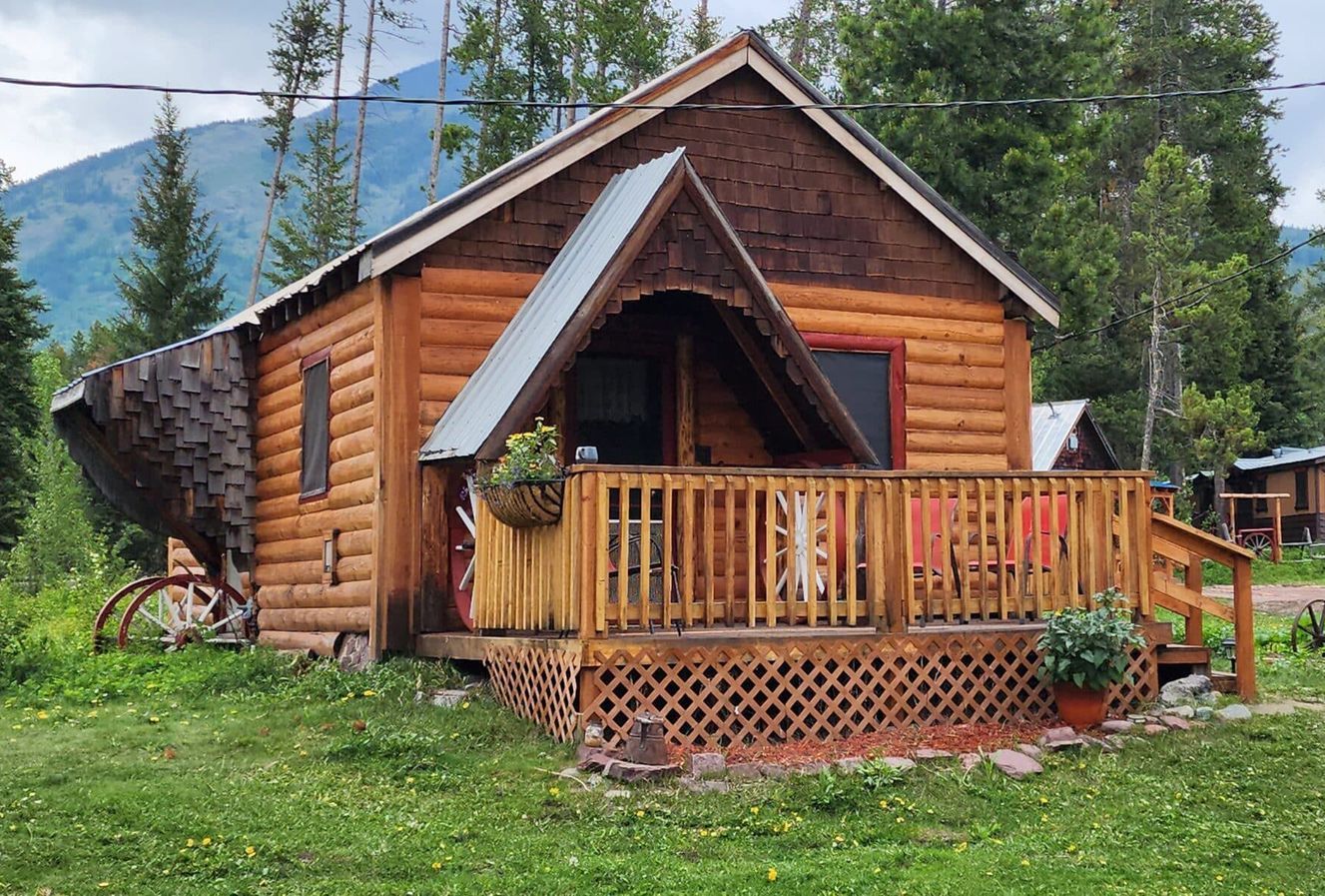 A small log cabin with a porch and mountains in the background.