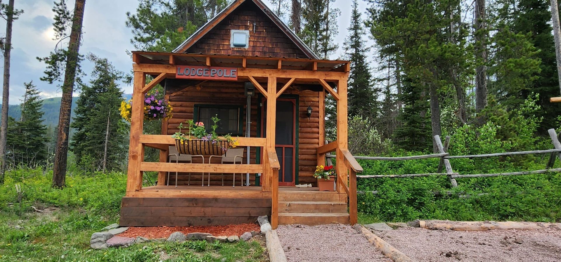 A small wooden cabin with a porch in the middle of a forest.