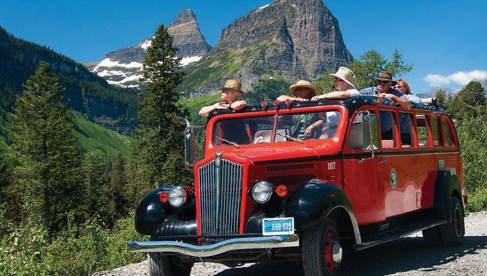 A red bus with a mountain in the background is driving down a dirt road.