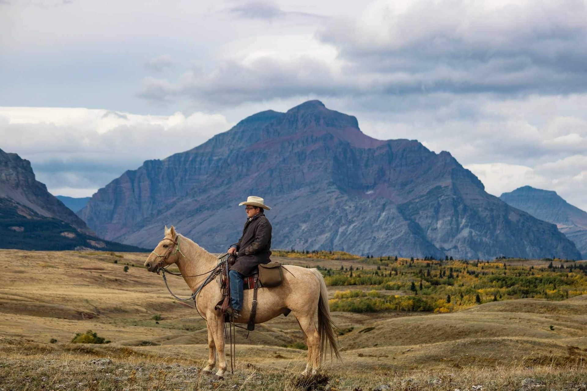 A group of people are riding horses in a field with mountains in the background.