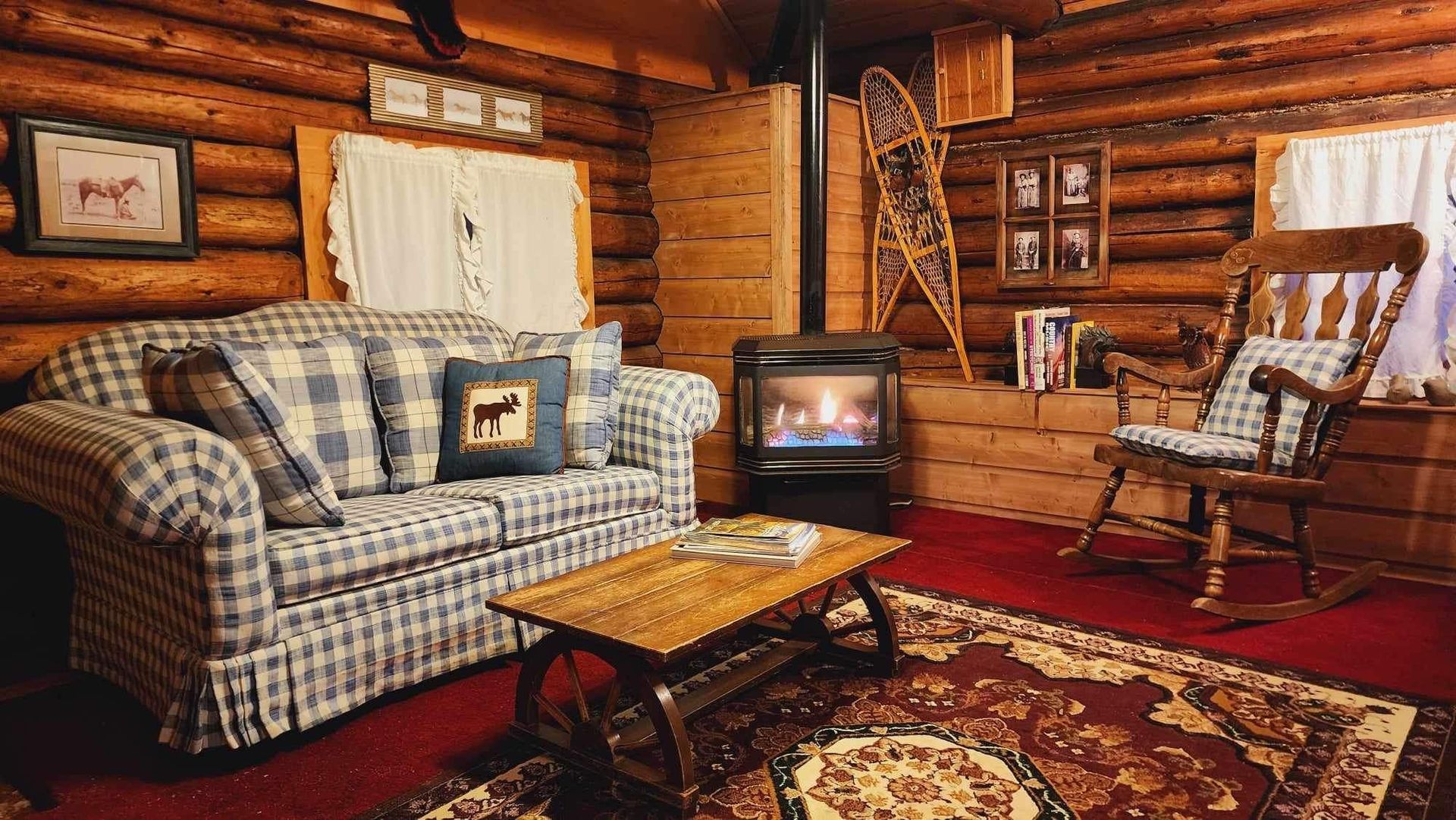 A living room in a log cabin with a couch , rocking chair , coffee table and fireplace.