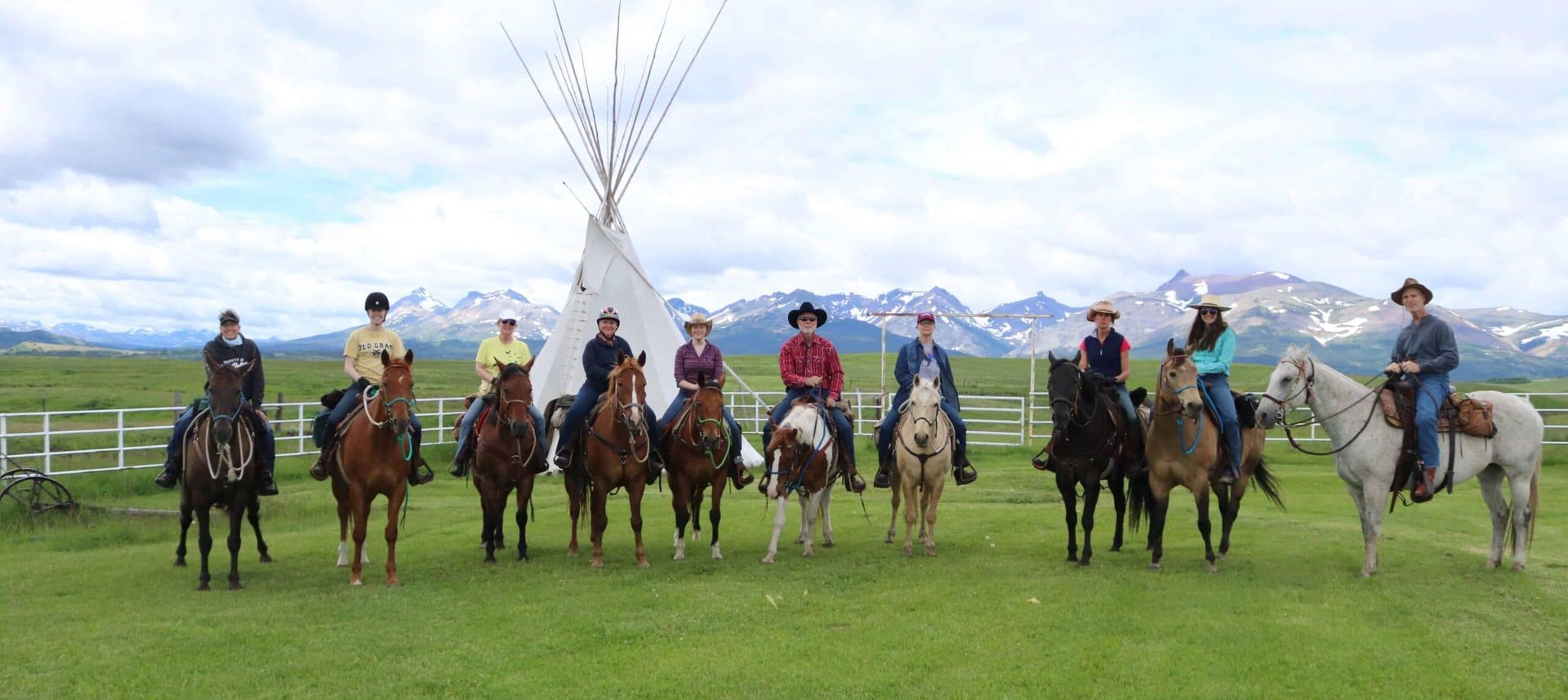 A group of people are riding horses in a field in front of a teepee.