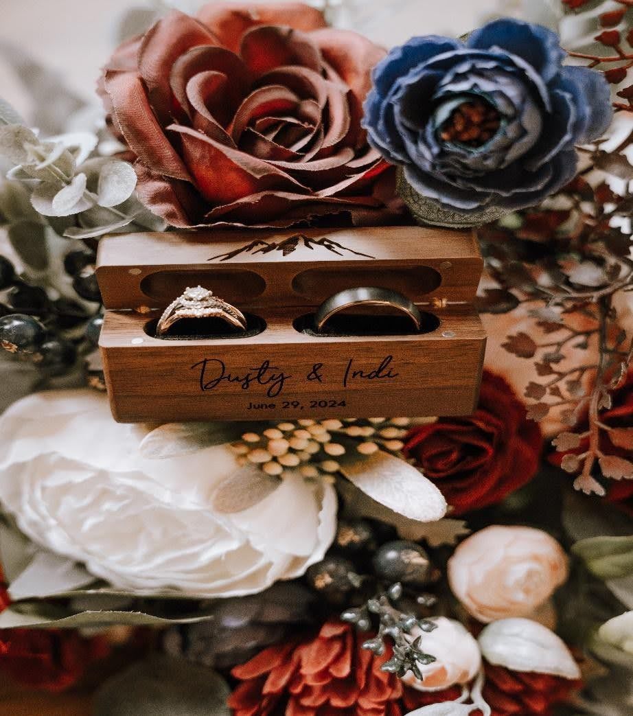 The wedding rings are in a wooden box surrounded by flowers.