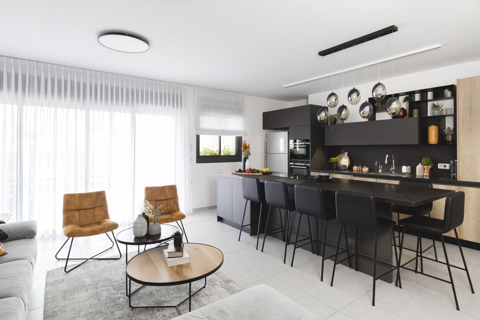 הלבשת חלל סלון ומטבח בגווני אפור שחור וחרדל. שפע של צמחים.  שחור-אפור וכל מה שבניהם בעיצוב של מעצבת פנים ומלבישה בתים ג׳ני ויאליך jenyvstudio