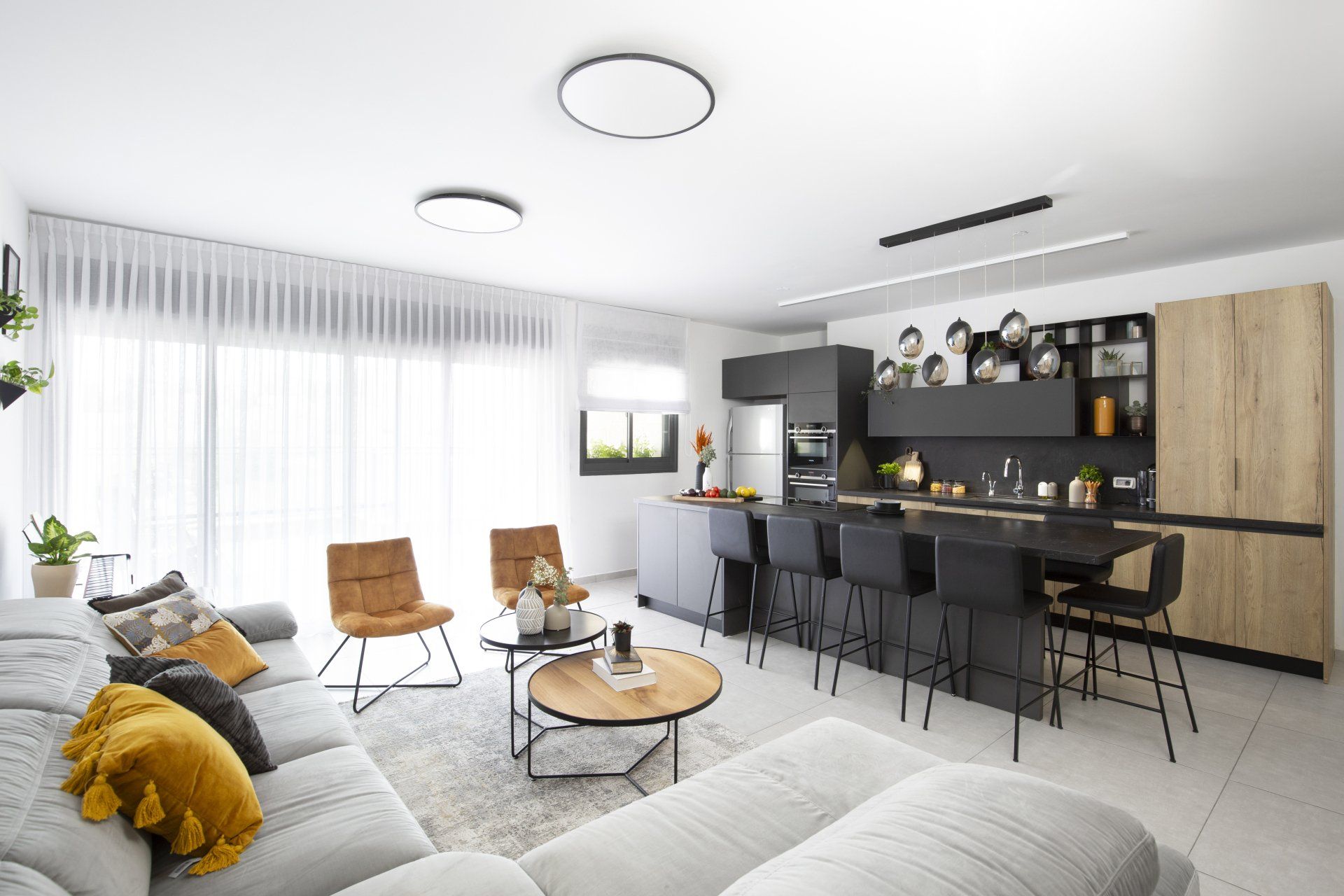 הלבשת חלל סלון ומטבח בגווני אפור שחור וחרדל. שפע של צמחים.  שחור-אפור וכל מה שבניהם בעיצוב של מעצבת פנים ומלבישה בתים ג׳ני ויאליך jenyvstudio