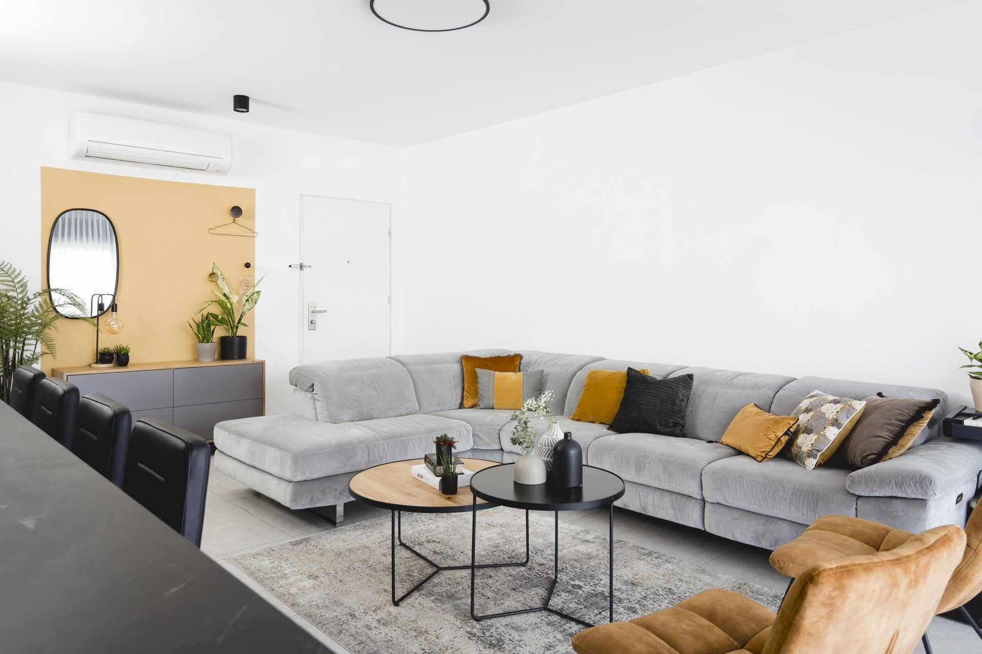 כריות נוי בצבע חרדל הלבשת חלל סלון ומטבח בגווני אפור שחור וחרדל. שפע של צמחים.  שחור-אפור וכל מה שבניהם בעיצוב של מעצבת פנים ומלבישה בתים ג׳ני ויאליך jenyvstudio