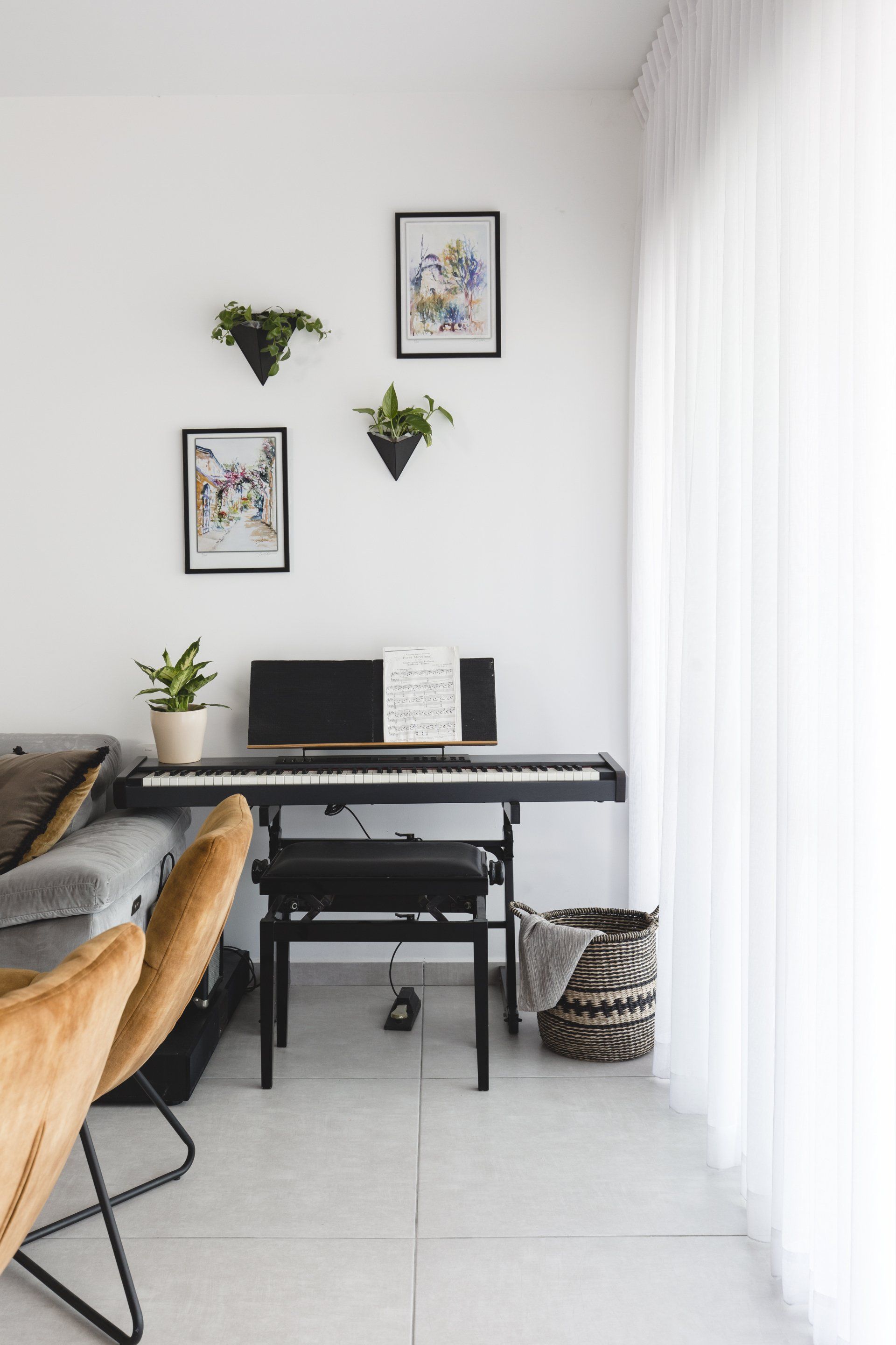 פינת מוזיקה עם פסנטר חשמלי הלבשת חלל סלון ומטבח בגווני אפור שחור וחרדל. שפע של צמחים.  שחור-אפור וכל מה שבניהם בעיצוב של מעצבת פנים ומלבישה בתים ג׳ני ויאליך jenyvstudio
