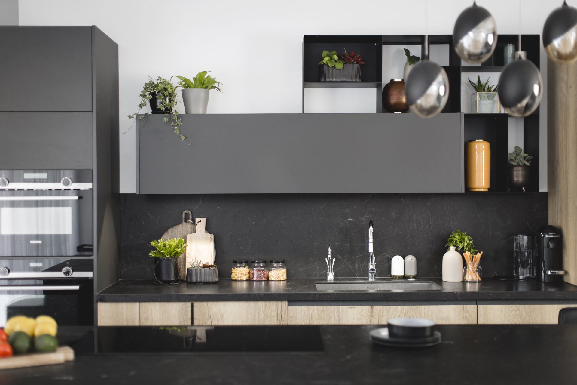 הלבשת חלל סלון ומטבח בגווני אפור שחור וחרדל. שפע של צמחים.  שחור-אפור וכל מה שבניהם בעיצוב של מעצבת פנים ומלבישה בתים ג׳ני ויאליך jenyvstudio