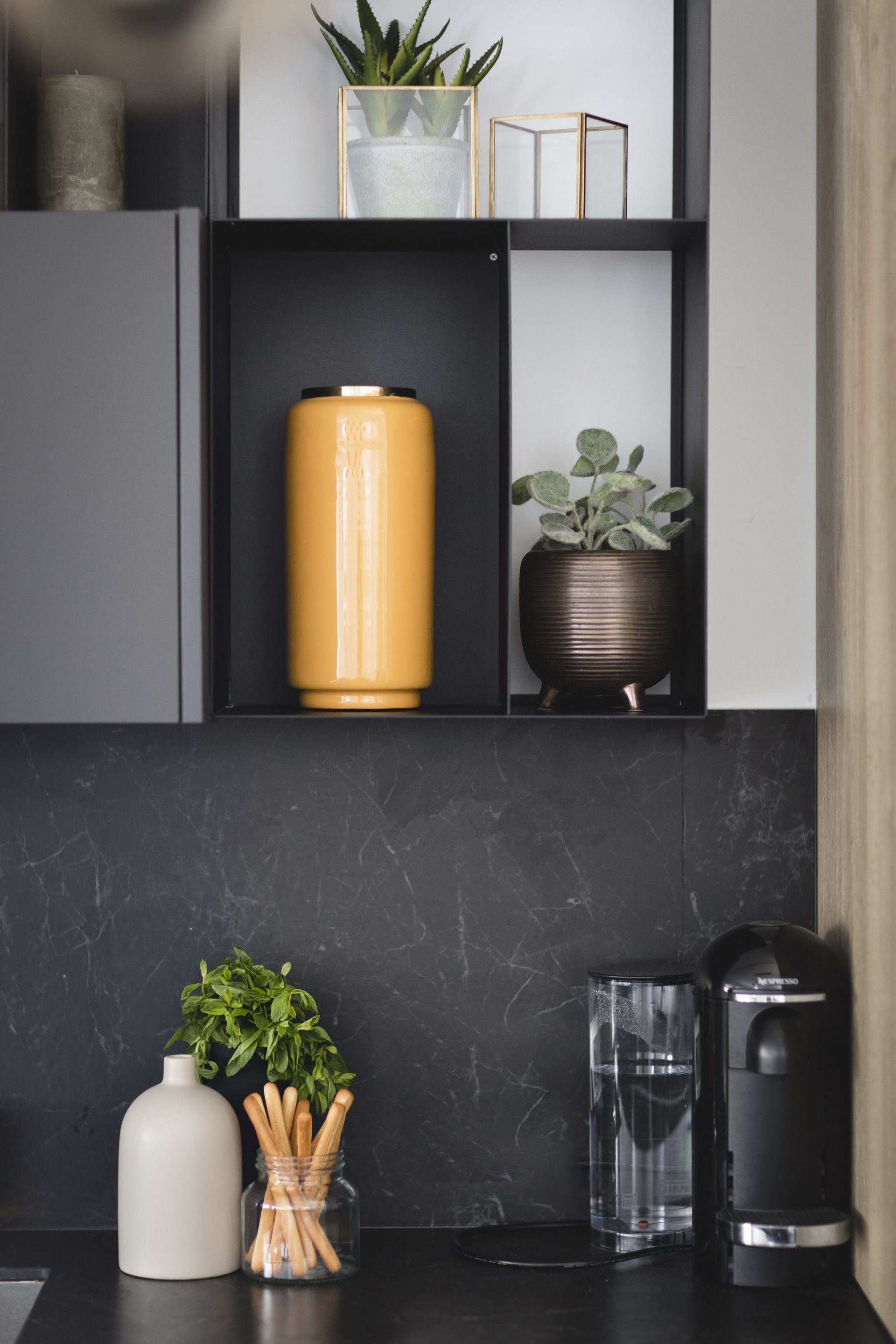 הלבשת חלל סלון ומטבח בגווני אפור שחור וחרדל. שפע של צמחים.  שחור-אפור וכל מה שבניהם בעיצוב של מעצבת פנים ומלבישה בתים ג׳ני ויאליך jenyvstudio