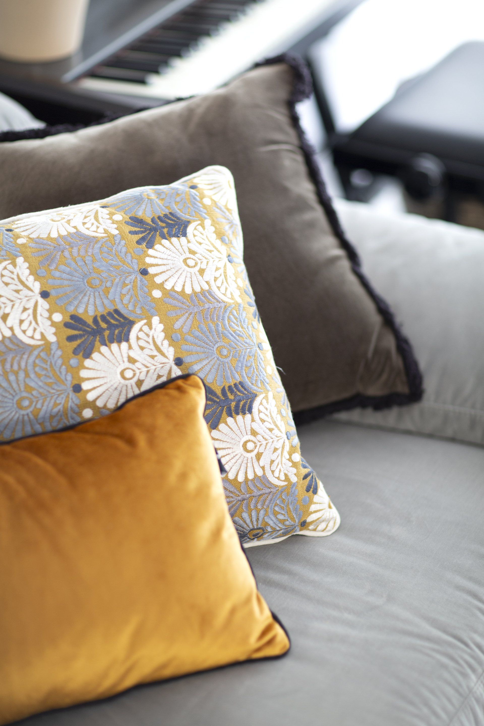 כריות נוי בצבע חרדל הלבשת חלל סלון ומטבח בגווני אפור שחור וחרדל. שפע של צמחים.  שחור-אפור וכל מה שבניהם בעיצוב של מעצבת פנים ומלבישה בתים ג׳ני ויאליך jenyvstudio