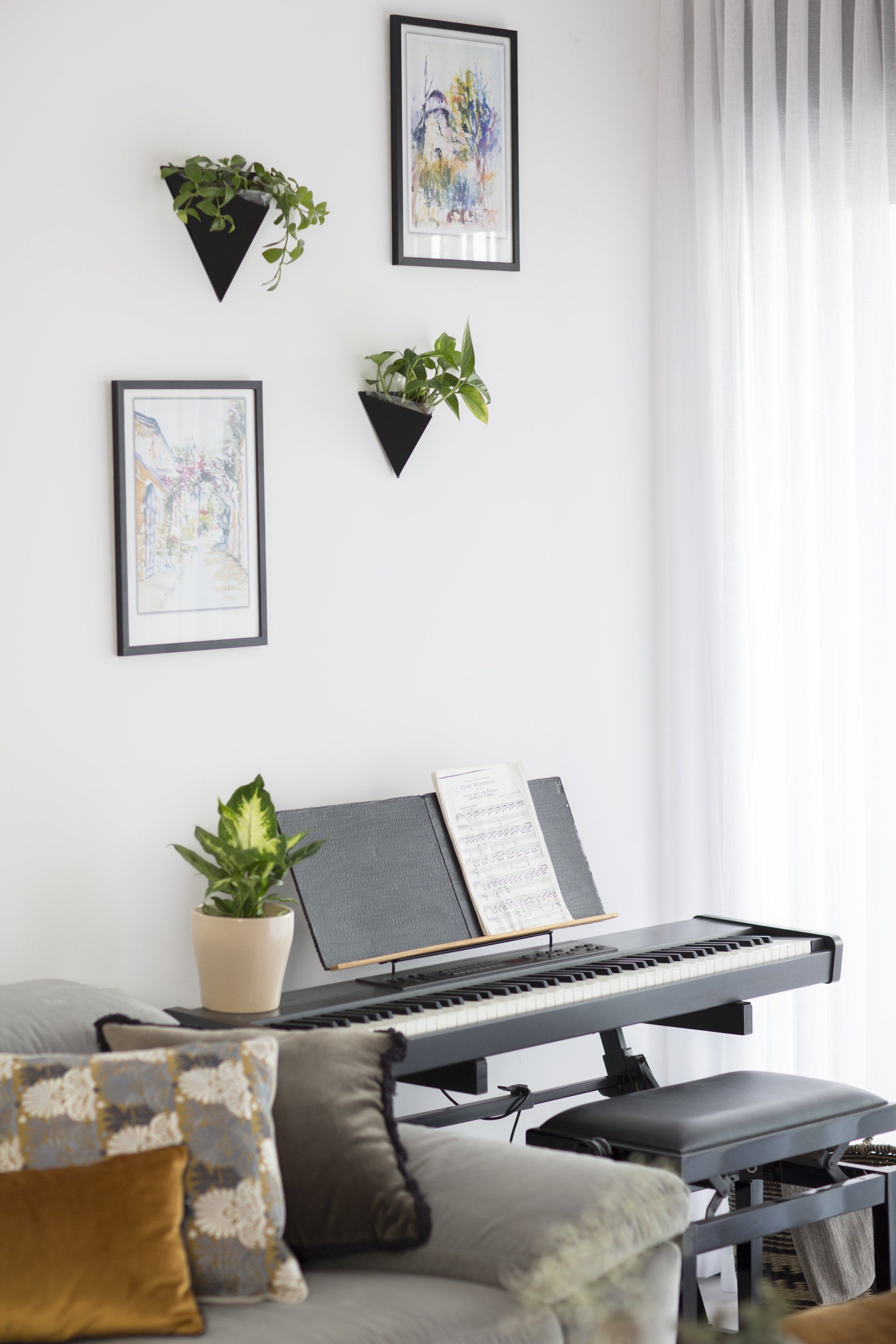 פינת מוזיקה עם פסנטר חשמלי הלבשת חלל סלון ומטבח בגווני אפור שחור וחרדל. שפע של צמחים.  שחור-אפור וכל מה שבניהם בעיצוב של מעצבת פנים ומלבישה בתים ג׳ני ויאליך jenyvstudio