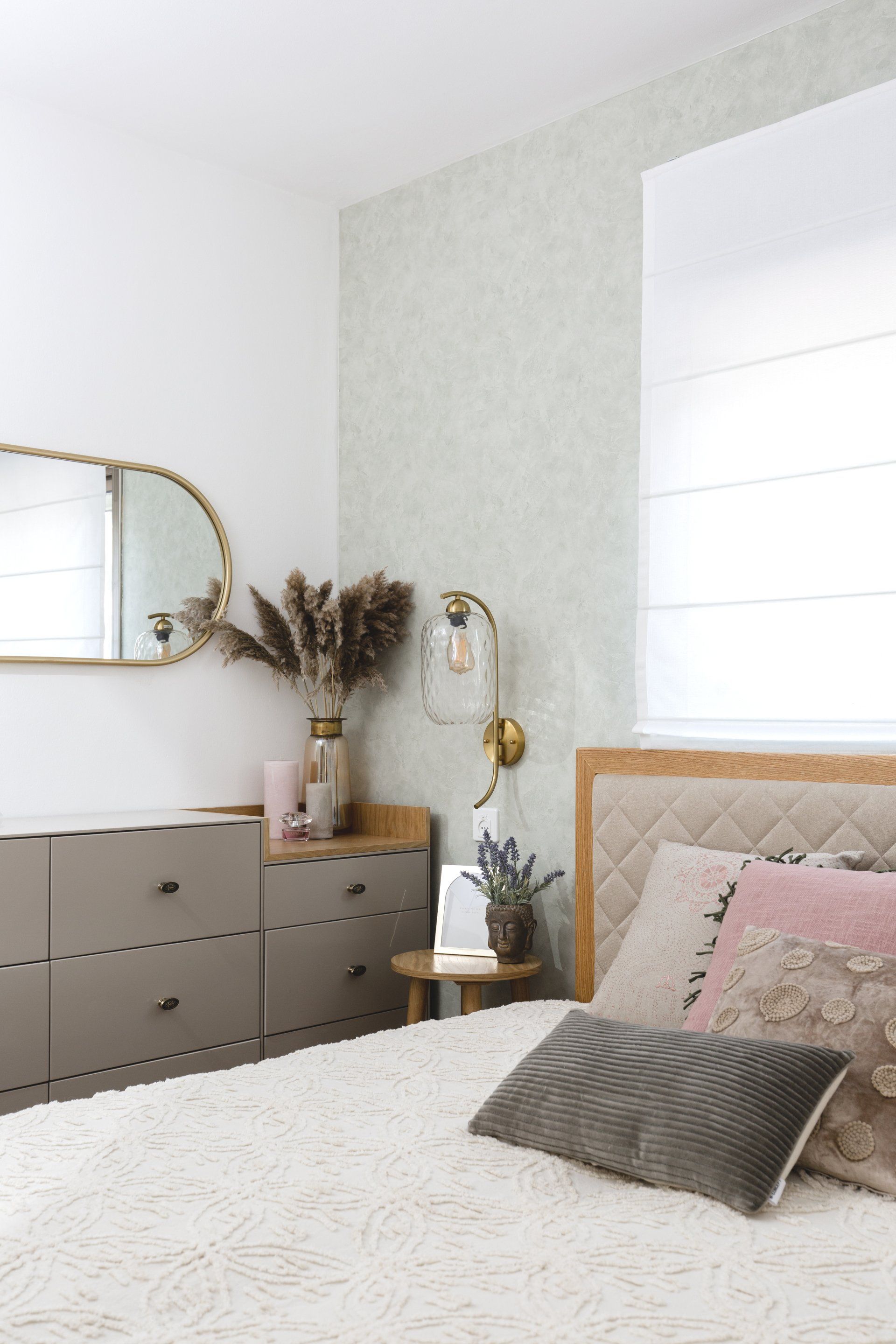 חדר שינה בגוונים רכים עם מראה אליפטית ואגרטל מעל שידה