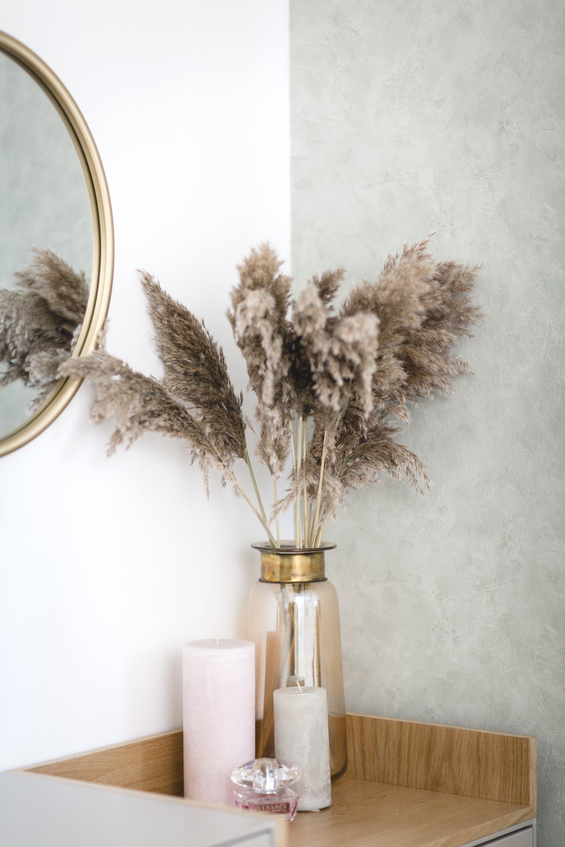 אגרטל צמחי פמפאס בגוון אפור לצד מראה מעוגלת עם שוליים מזהב