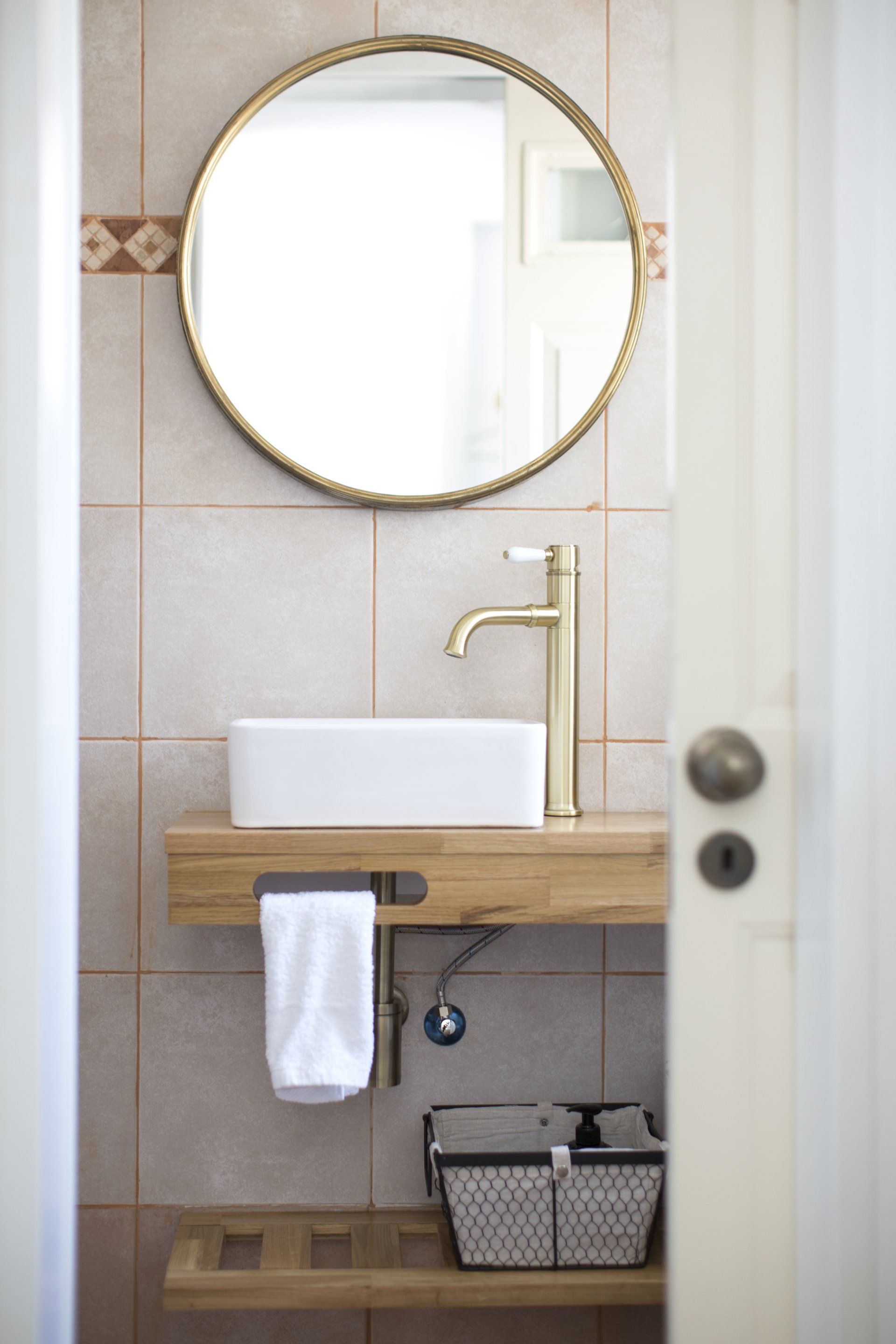 יחידת אמבטיה מעץ טבעי עם כיור לבן ומראה עגולה שתלוייה על הקיר